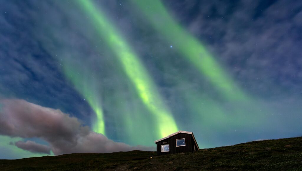 Cozy wooden house beneath vibrant Northern Lights with snowy landscape in a remote Arctic setting