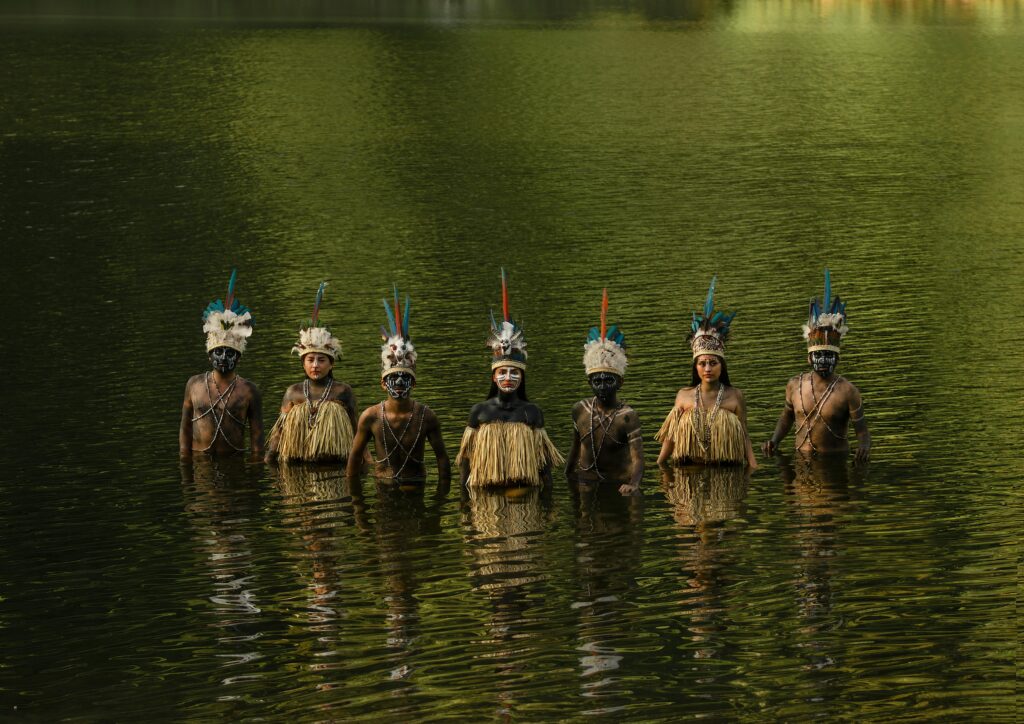 Indigenous people of the Amazon Rainforest standing in a peaceful lake, wearing traditional attire and feathered headdresses