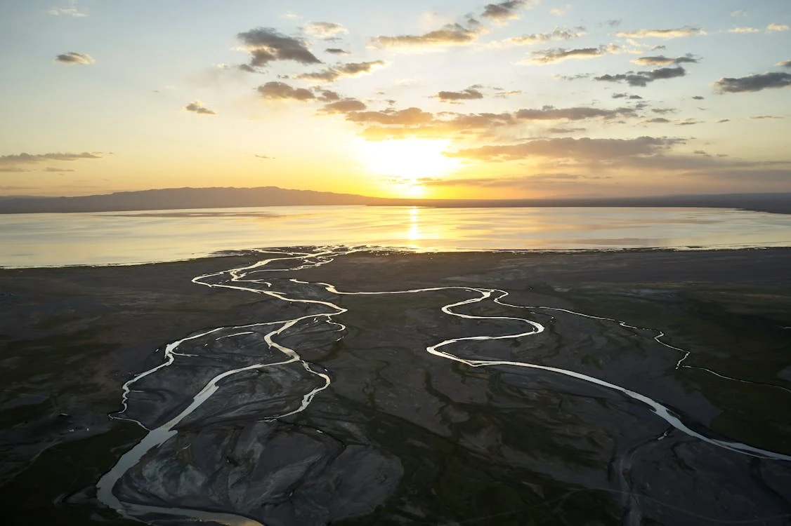 Meandering river flowing into a serene lake at sunset with golden reflections on the water and distant mountains on the horizon in Mongolia
