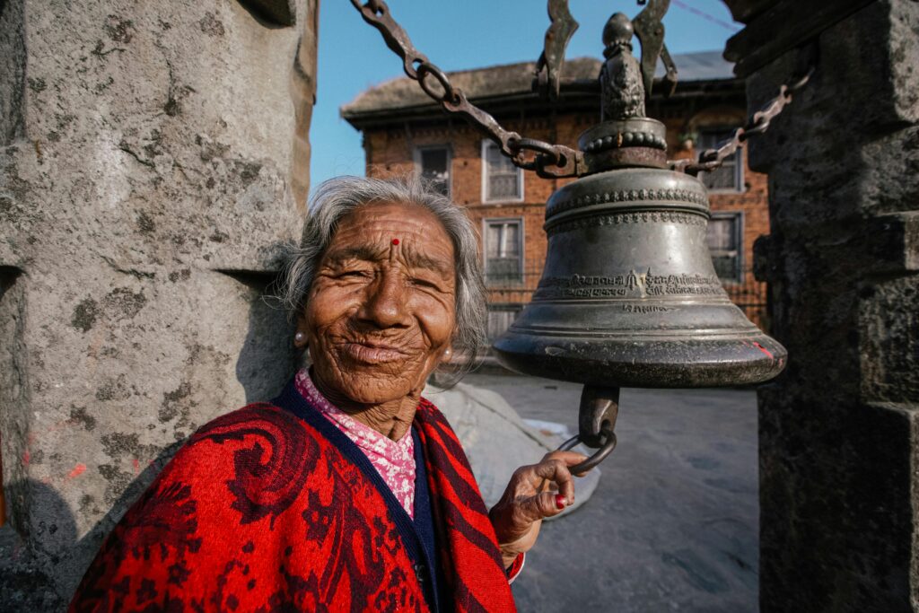 Elderly Nepali woman in Bhaktapur gently ringing a traditional metal bell, surrounded by ancient temples - best places to visit in Nepal