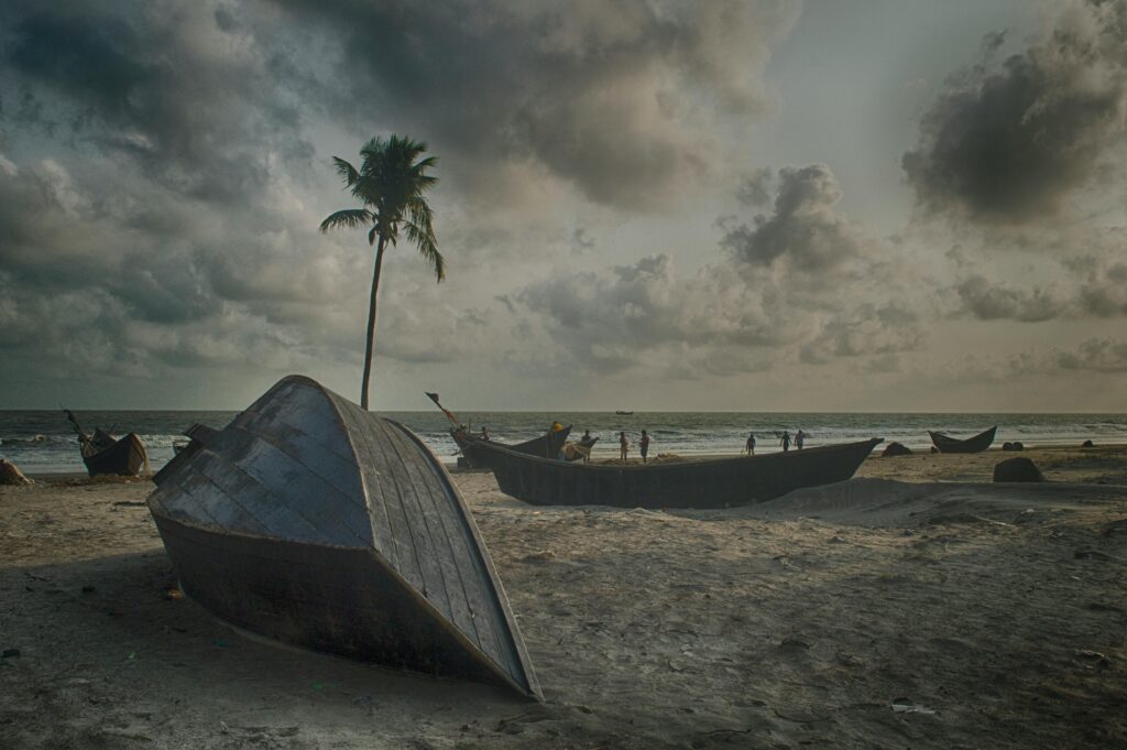 People and fishing boat on the sandy shore of Cox's Bazar Beach, Bangladesh, under a cloudy sky with moody coastal atmosphere