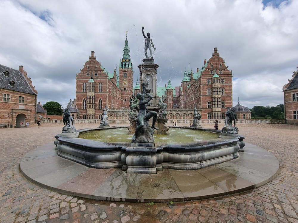 Neptune Fountain in the courtyard of Frederiksborg Castle, Hillerød, Denmark, with Renaissance architecture and dramatic cloudy sky in the background