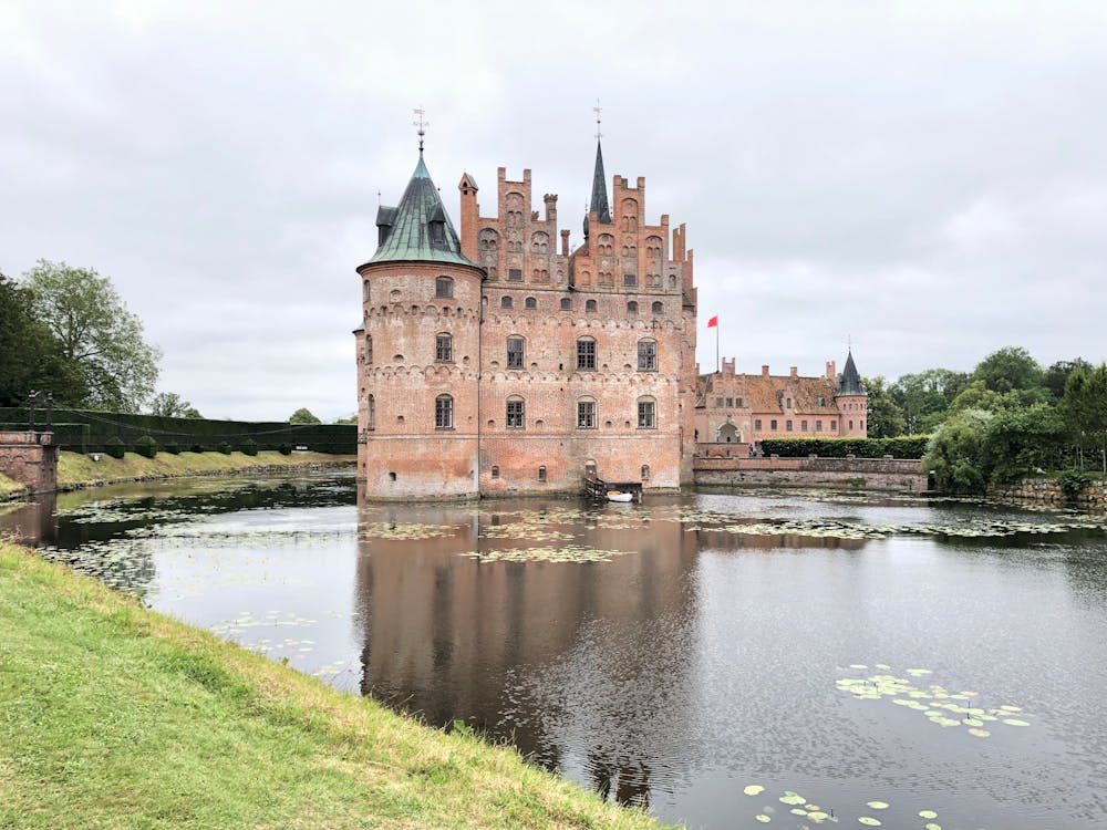 Egeskov Castle in Denmark surrounded by a moat and lush greenery, showcasing Renaissance architecture on a cloudy day
