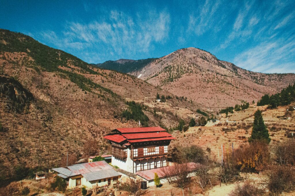 Traditional red-roofed house in Haa Valley, Bhutan, surrounded by majestic green mountains and serene alpine landscapes.