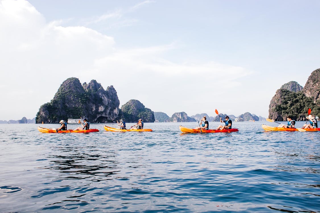 Person kayaking through the emerald waters of Ha Long Bay, surrounded by towering limestone karsts