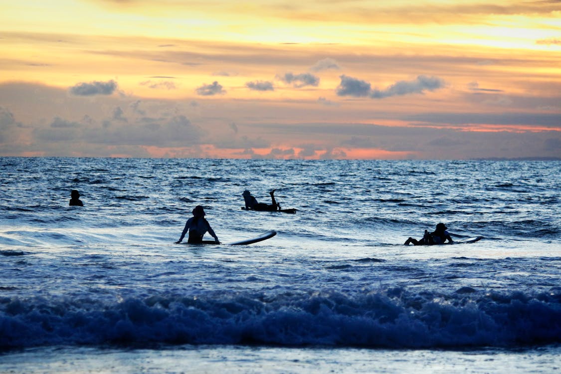 Surfers enjoying a stunning sunrise at Kuta Beach with golden skies and ocean waves