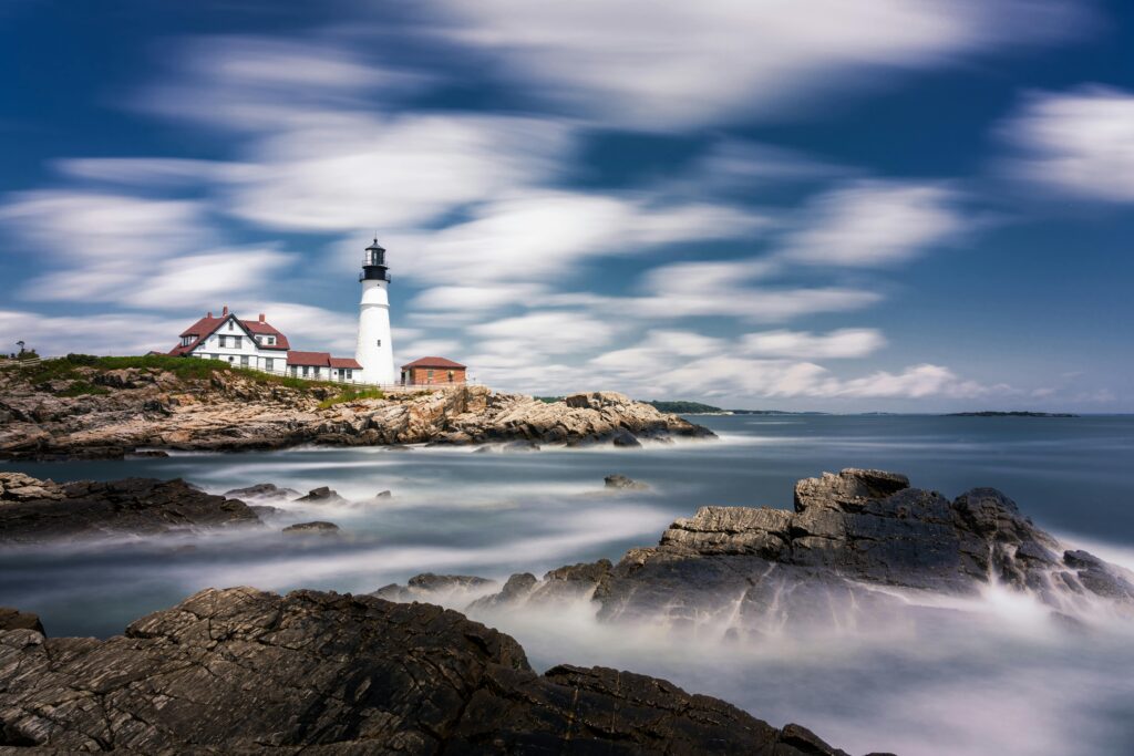 Scenic view of Portland Head Light lighthouse on a rocky Maine coastline with dramatic clouds and smooth ocean waves captured in long exposure