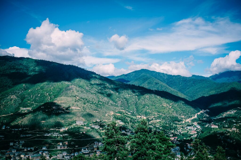 Panoramic view of lush green mountains and valley near Thimphu, Bhutan, under a bright blue sky with scattered clouds