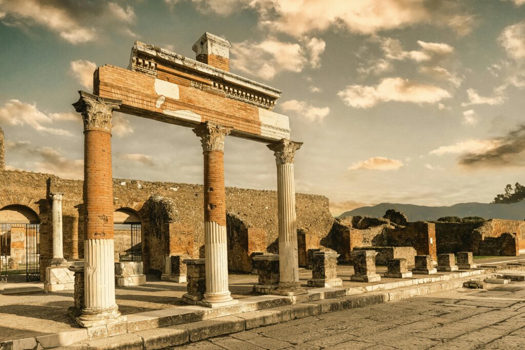Ancient Roman ruins in Pompeii, Italy, featuring partially restored columns and archways under a dramatic sunset sky