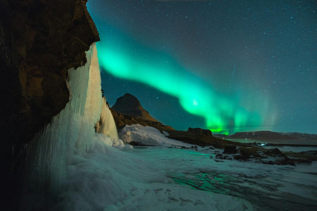 Seljalandsfoss Waterfall illuminated under the Northern Lights with a starry night sky in Iceland’s scenic countryside