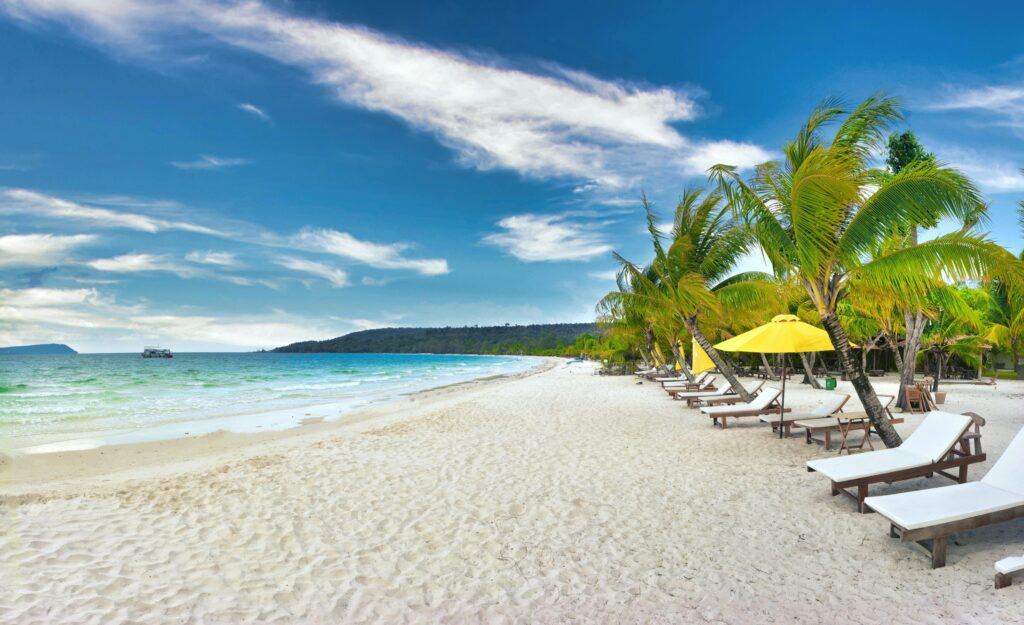 Tropical beach in Sihanoukville, Cambodia, with coconut trees, relaxing beach chairs, and a clear blue sky overlooking the calm ocean