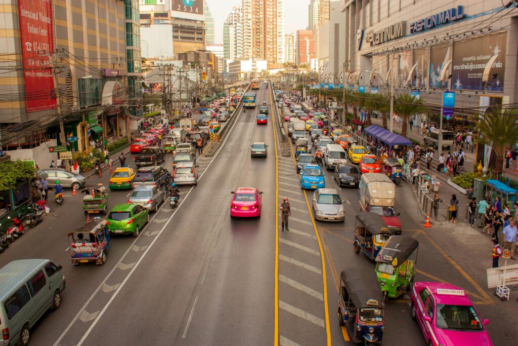 Busy street scene in Bangkok, Thailand, with colorful taxis, tuk-tuks, and motorbikes in front of Platinum Fashion Mall during rush hour.