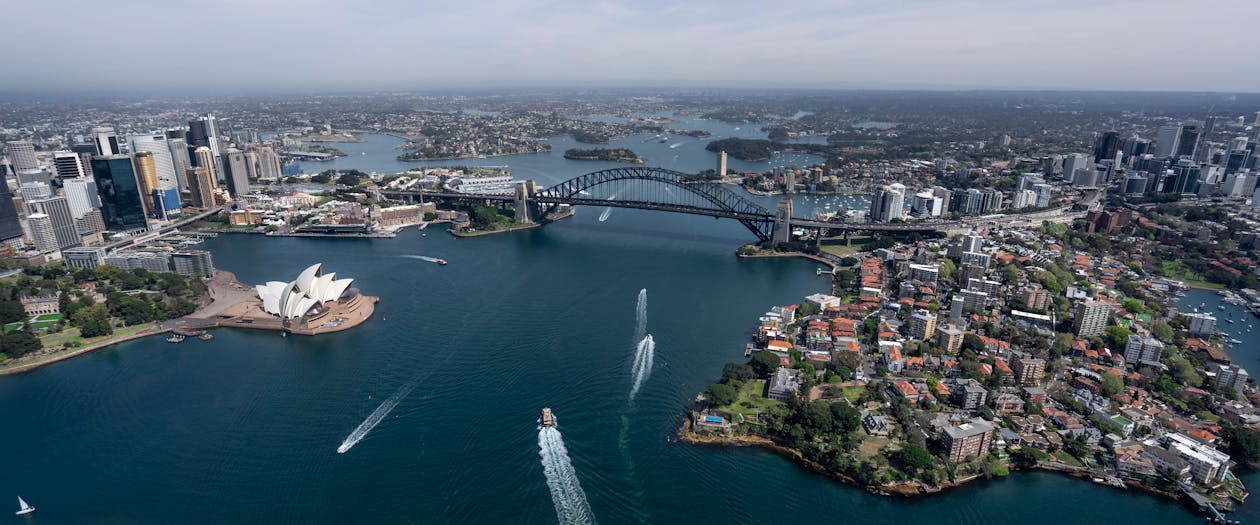 Aerial view of Port Jackson in Sydney, showcasing the iconic Sydney Harbour Bridge, Opera House, and sparkling blue waters