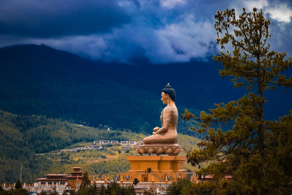 Buddha Dordenma statue overlooking the lush mountains of Thimphu, Bhutan, under a dramatic sky surrounded by pine trees