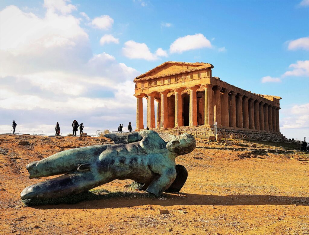 Fallen ancient Greek statue in the Valley of the Temples, Agrigento, Sicily, with temple ruins in the background
