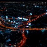 A nighttime view of Bangkok with illuminated avenues and towering skyscrapers in the city center.