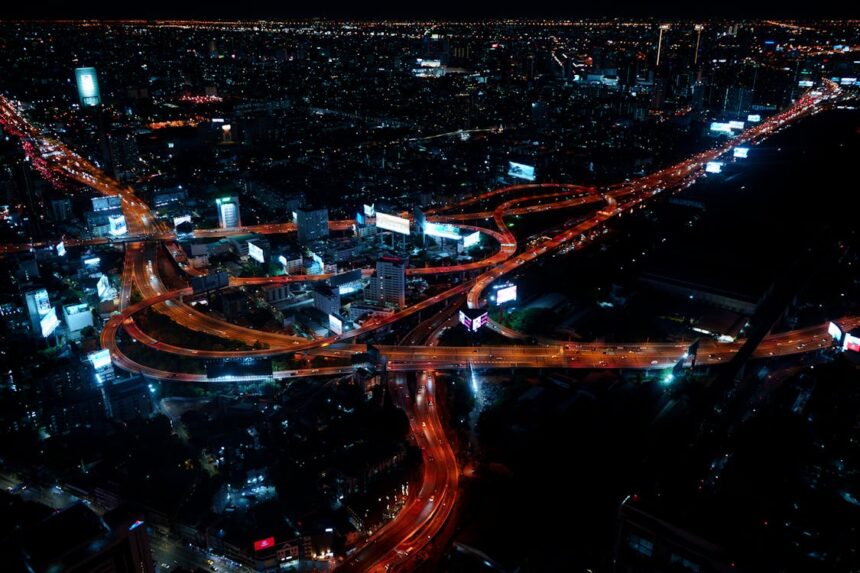 A nighttime view of Bangkok with illuminated avenues and towering skyscrapers in the city center.