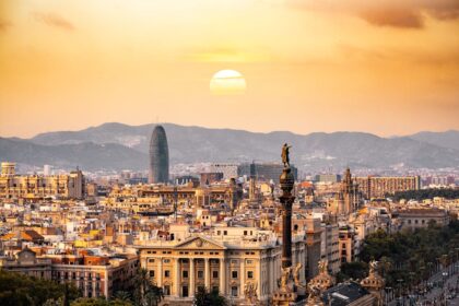A stunning sunset view of Barcelona, featuring the Columbus Monument in the foreground, historic architecture, and the modern Torre Glòries skyscraper