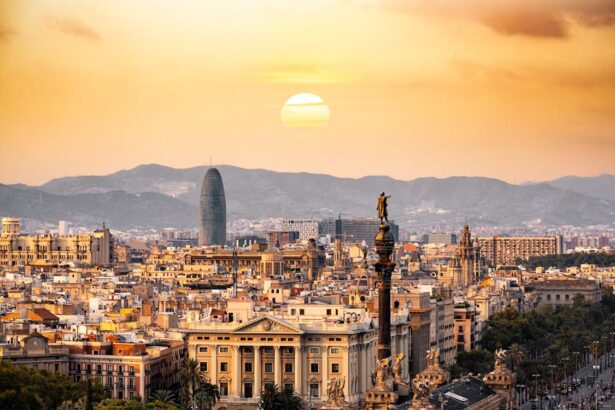 A stunning sunset view of Barcelona, featuring the Columbus Monument in the foreground, historic architecture, and the modern Torre Glòries skyscraper