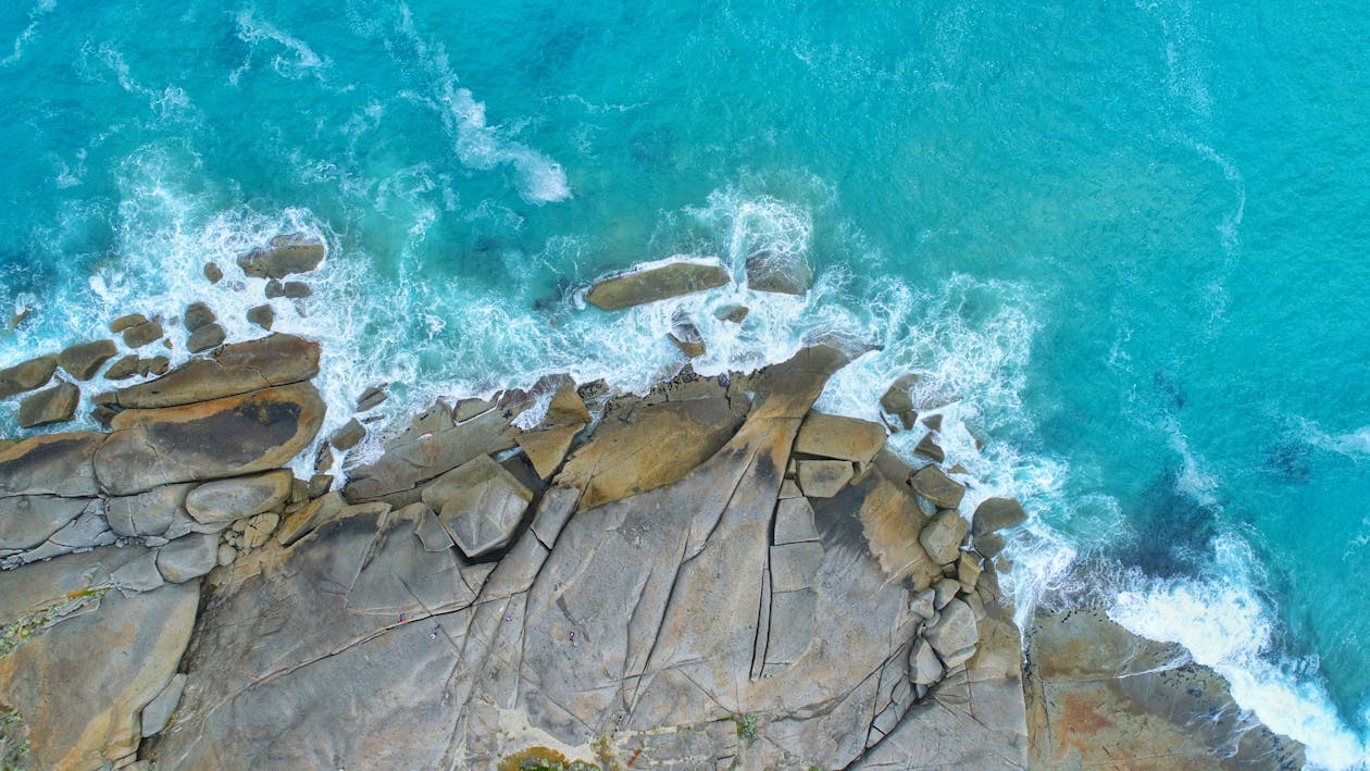 Aerial shot of powerful ocean waves crashing against rugged coastal rocks with white sea foam and deep blue water