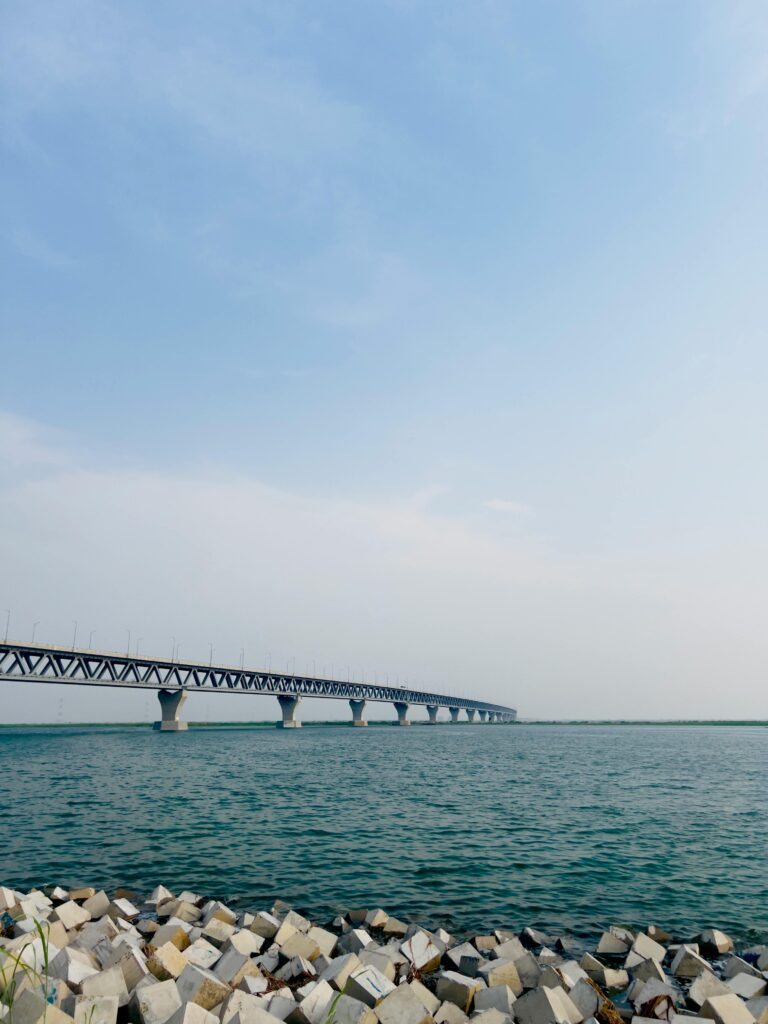 Panoramic view of Padma Bridge stretching across the Padma River in Bangladesh, with calm water and a cloudy sky in the background