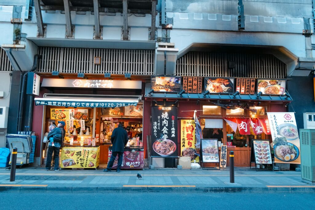 Local Japanese restaurants under railway tracks with colorful signs and people ordering food  