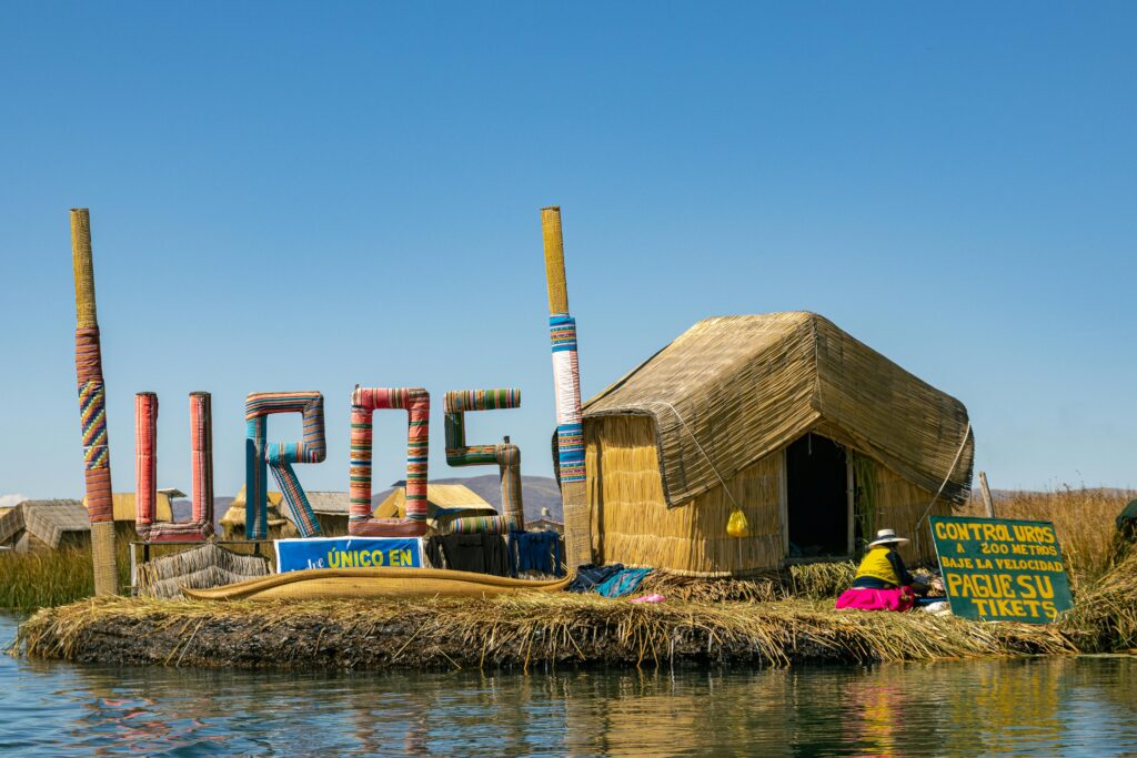 Traditional Uros floating island on Lake Titicaca with reed huts, colorful signage, and locals in traditional attire under a clear blue sky