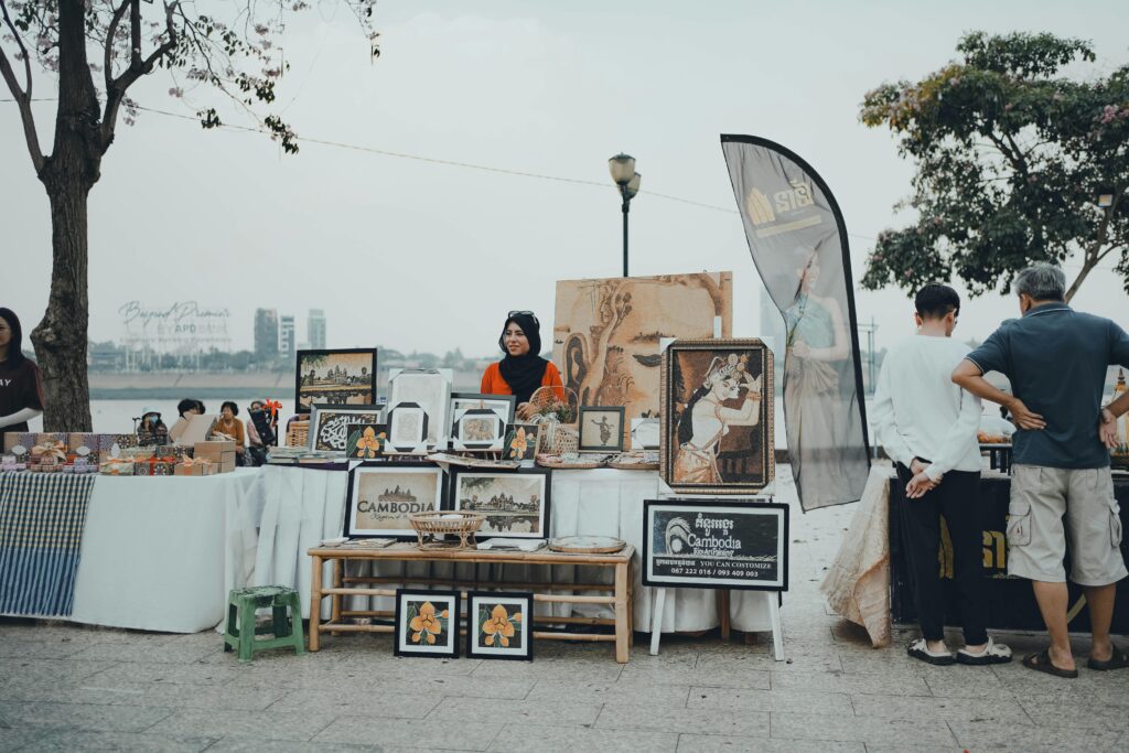 Woman selling artwork at a vibrant street market along the riverside in Phnom Penh, Cambodia, with colorful stalls