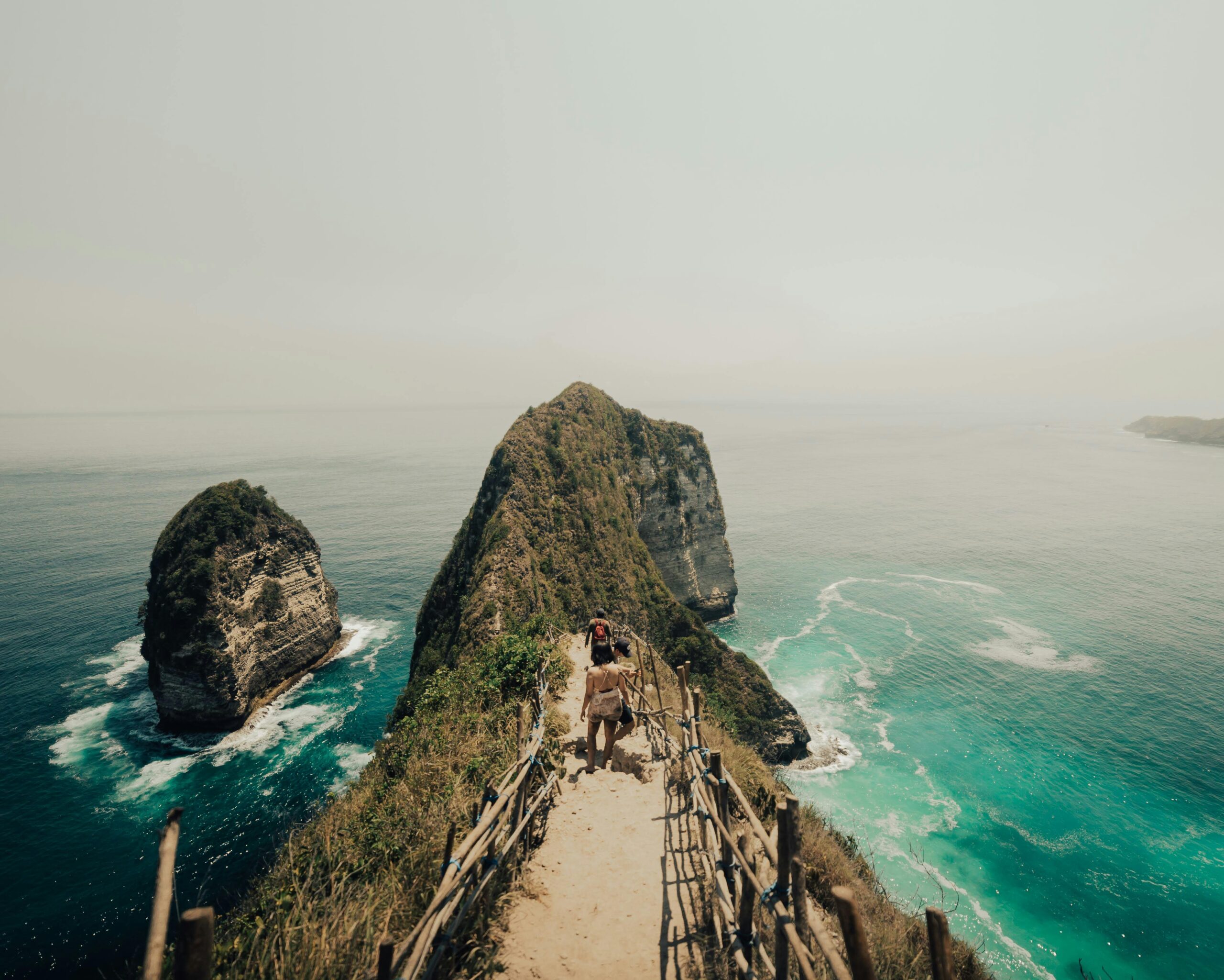 Tourists walking along the cliffside path at Kelingking Beach on Nusa Penida Island, overlooking turquoise waves and dramatic rock formations