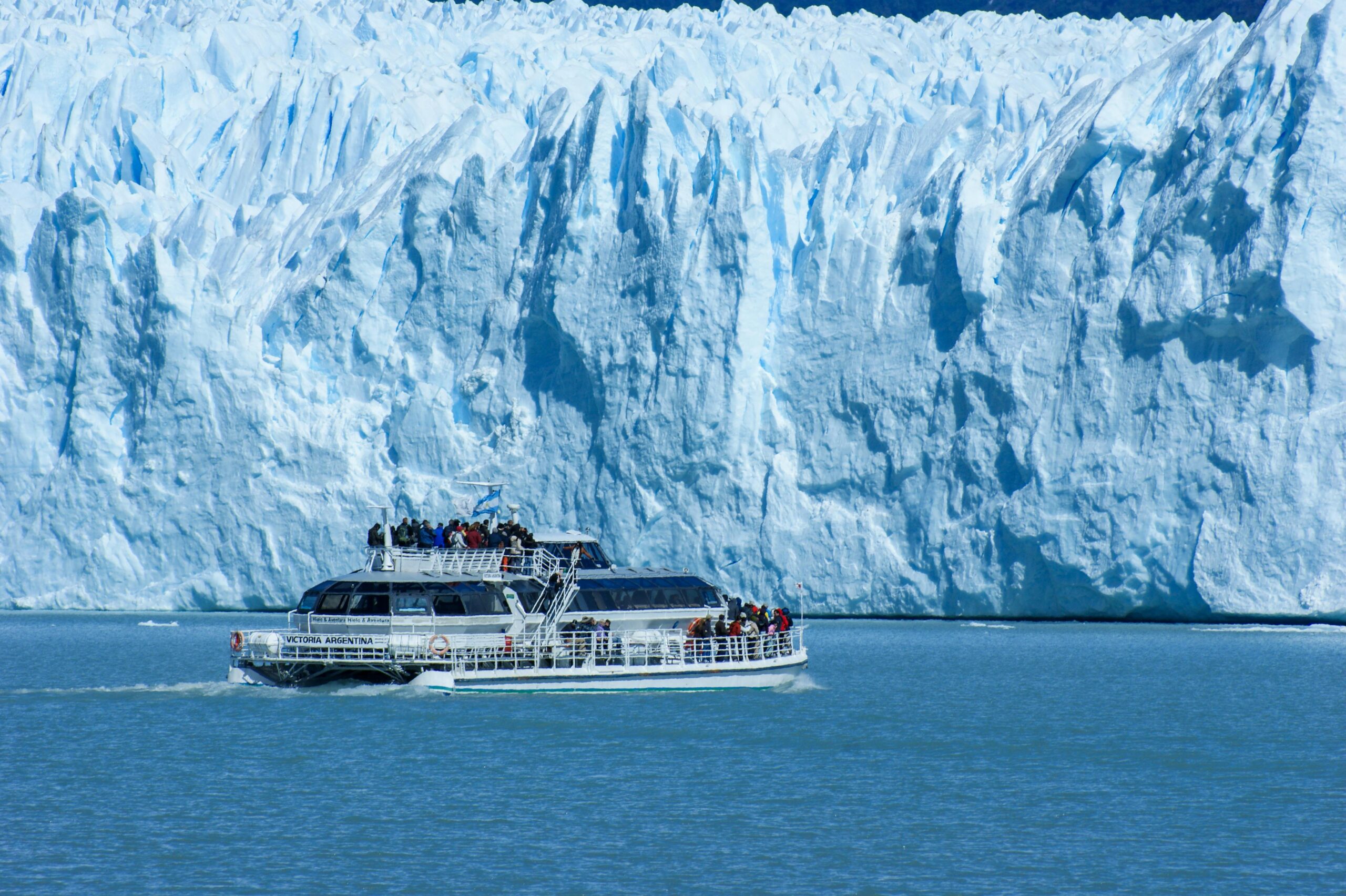 Tour boat filled with visitors cruising in front of the massive Perito Moreno Glacier in Patagonia, Argentina