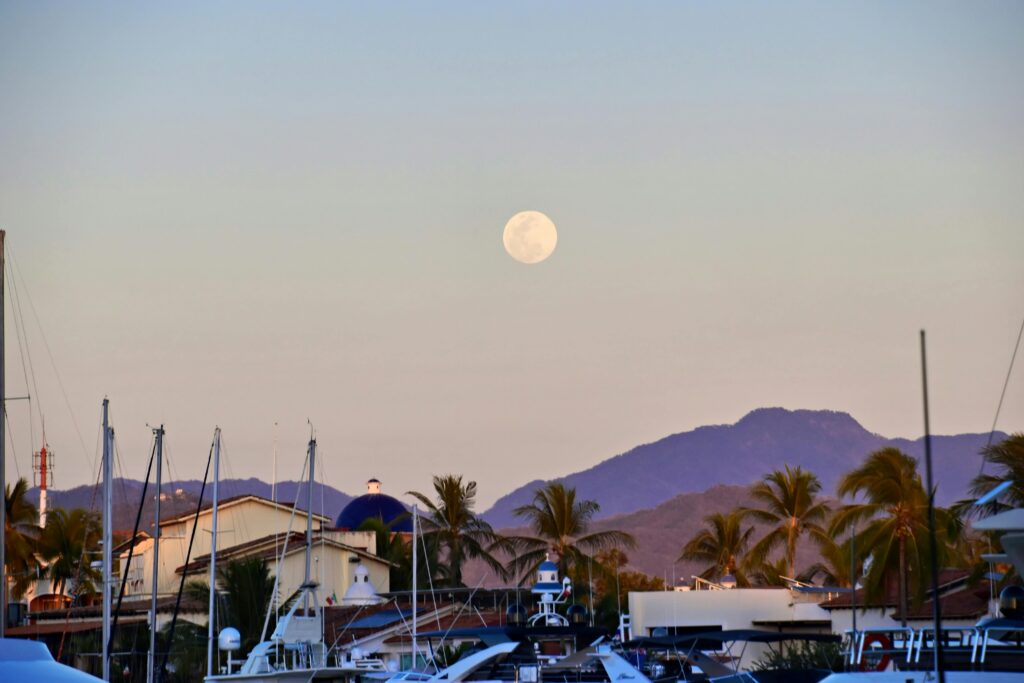 Full moon rising over mountains and marina with palm trees and boats in Puerto Vallarta, Mexico