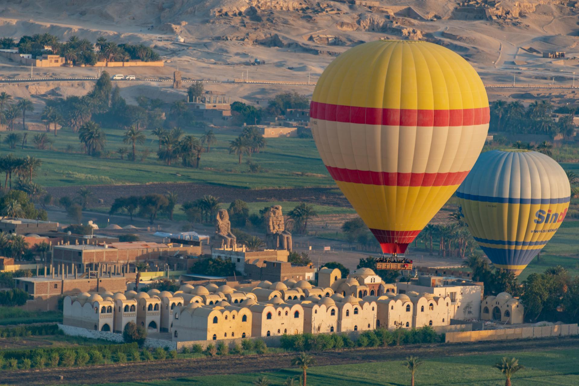 Hot air balloons flying over Luxor with view of Colossi of Memnon in the background