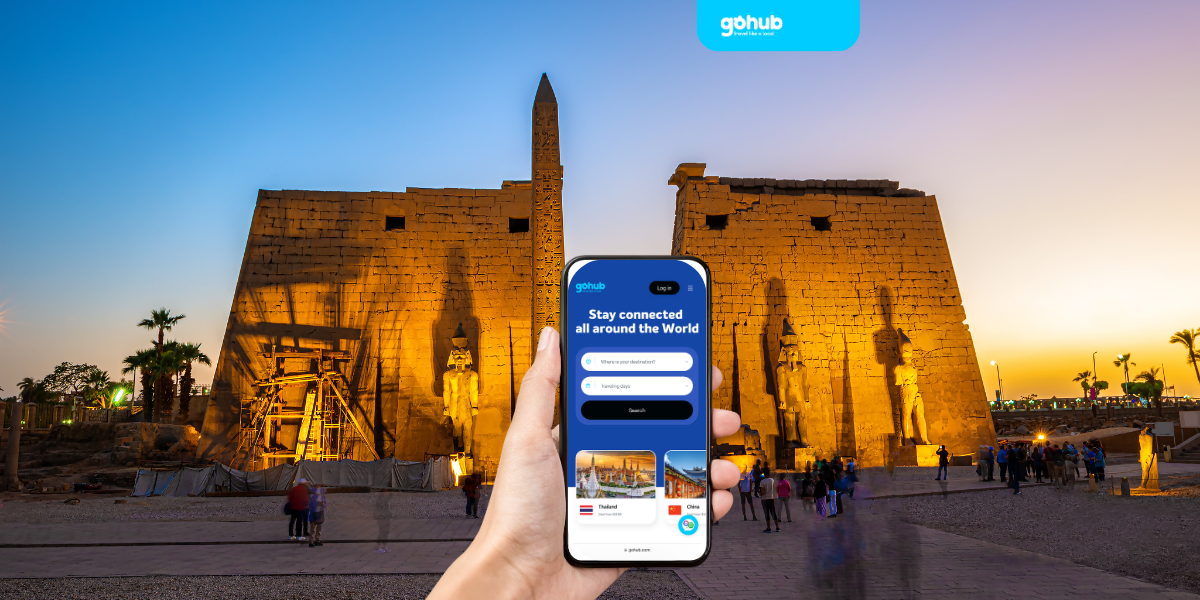Tourist holding phone with Gohub eSIM app in front of Luxor Temple at night