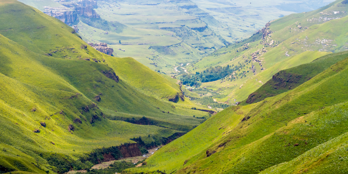 Scenic view of Lesotho's highland valley with green rolling hills and remote terrain, illustrating rural travel conditions.